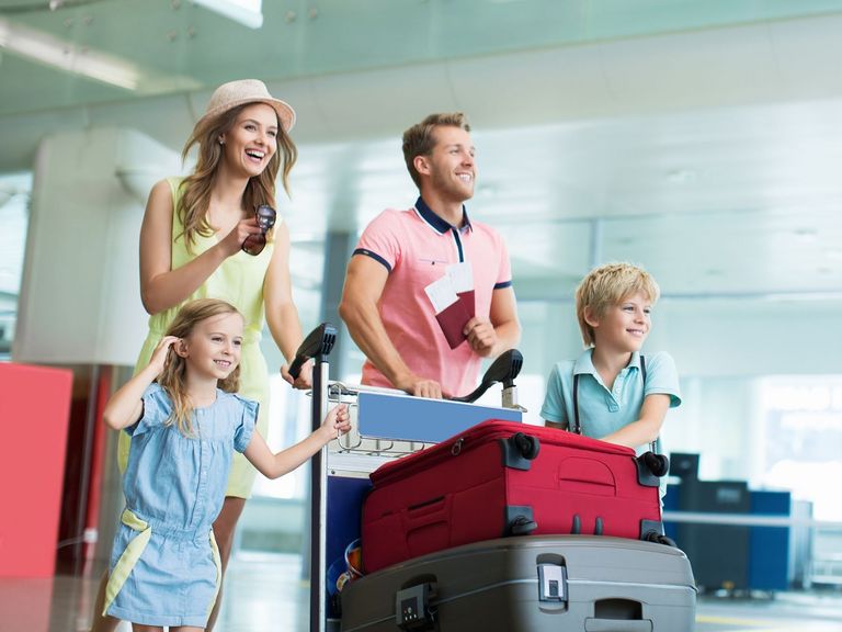 Vieköpfige Familie fährt schiebt einen Kofferwagen mit Koffern durch ein Flughafengebäude