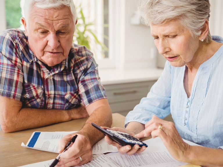 Rentnerpaar sitzen mit Taschenrechner und Stift an einem Tisch