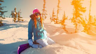 Junges Mädchen in Skiklamotten hockt im Schnee und lacht