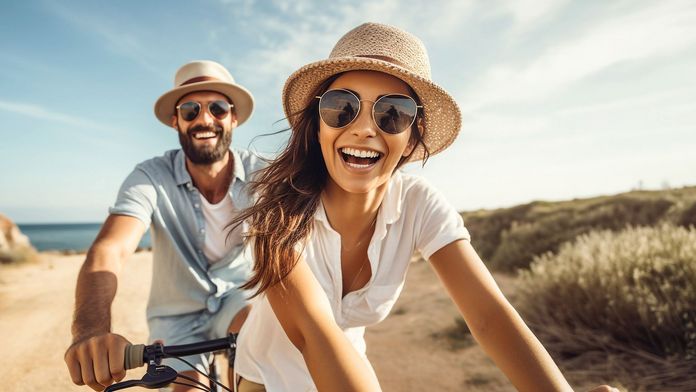 Lachendes Paar auf einem Tandem und mit Sonnenhüten