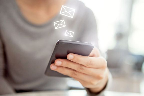 Frauenhand hält ein Smartphone und darüber schweben kleine Briefumschlagsymbole