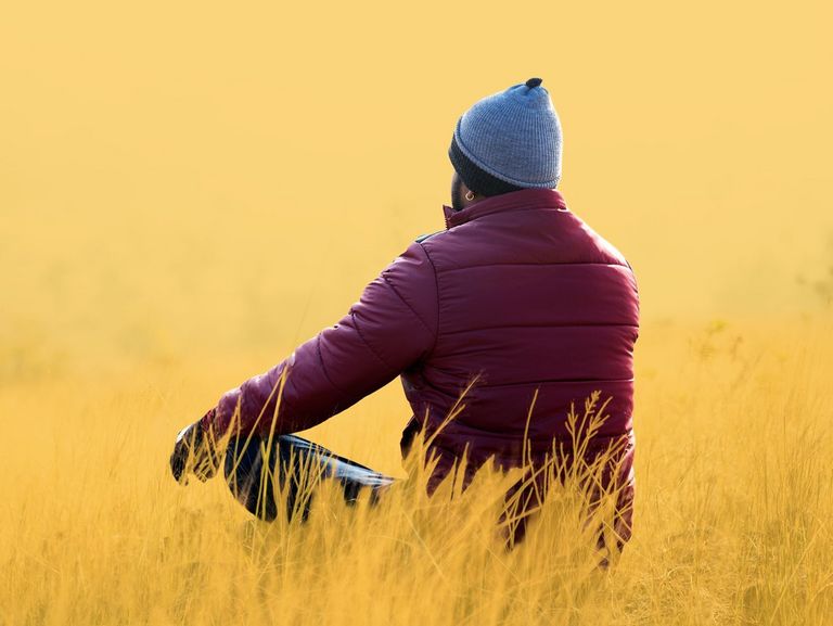 Mann sitzt im Lotussitz auf einer herbstlichen Wiese