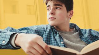 Jugendlicher sitzt verträumt auf einem Sofa und hält ein Buch