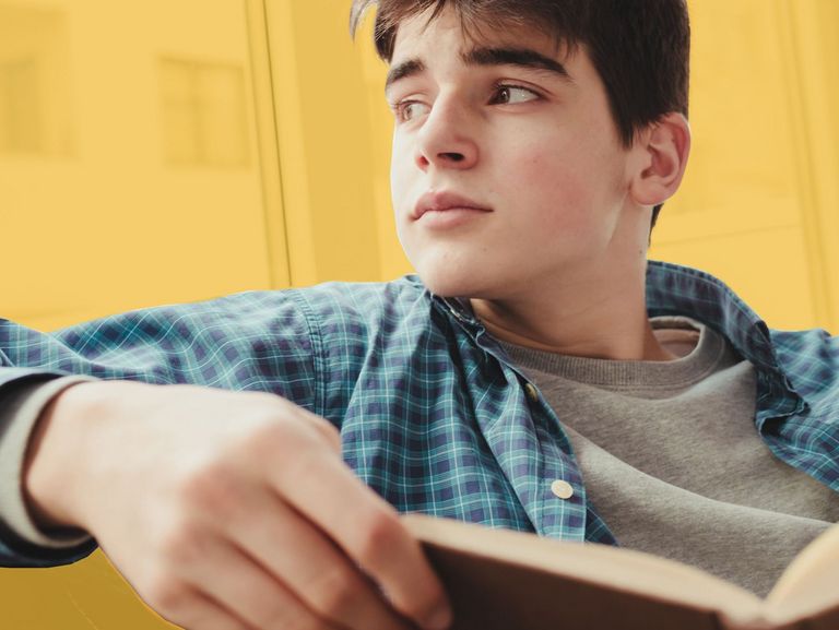 Jugendlicher sitzt verträumt auf einem Sofa und hält ein Buch