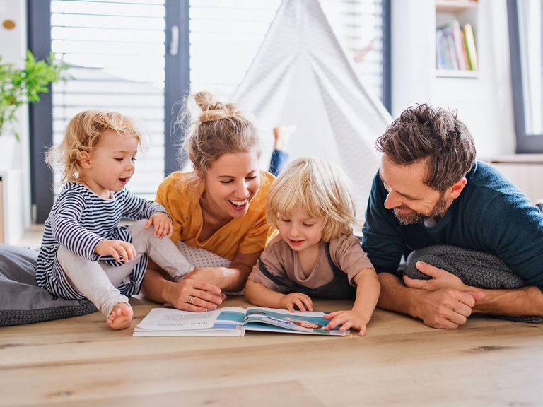 Familie mit 2 Kindern liest freudig Buch im Kinderzimmer auf dem Boden﻿