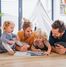 Familie mit 2 Kindern lesen im Kinderzimmer auf dem Fußboden gemeinsam mit viel Freude ein Buch