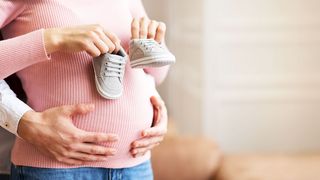 Mann hält den Babybauch einer Frau und diese hat Babyschuhe in der Hand