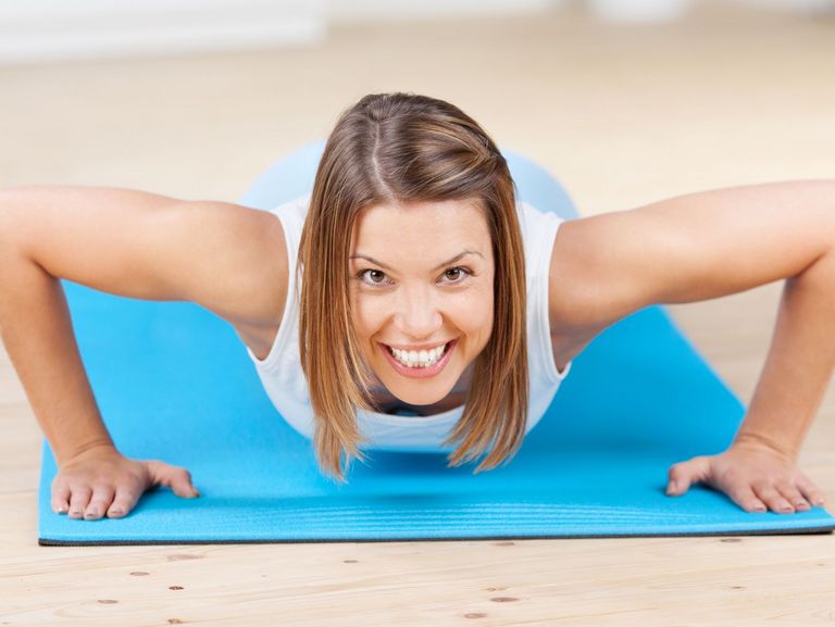 Frau macht einen Liegestütz auf einer blauen Matte und schaut in die Kamera