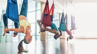 Gemischte Sportgruppe hängt Kopfüber in farbigen Yogatüchern, die an der Decke hängen