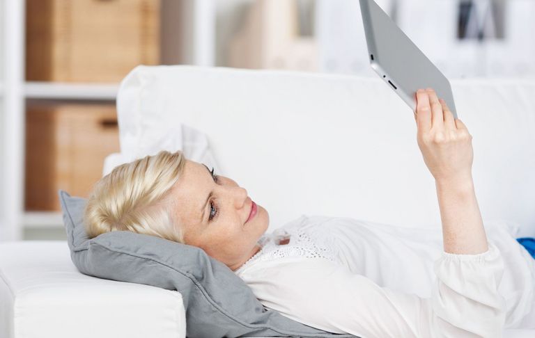 Frau liegt auf Sofa und liest auf Tablet