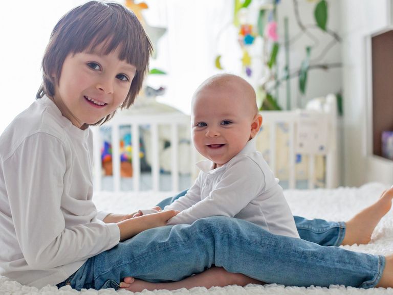 Schulkind und Baby sitzen auf einem Bett