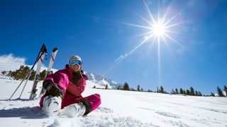 Frau sitzt im Schnee und im Hintergrund sind Ski und Skistöcke zu sehen