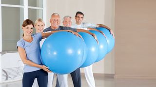 Gruppe mit Erwachsenen, bei der jeder einen großen, blauen Gymnastikball in der Hand hält