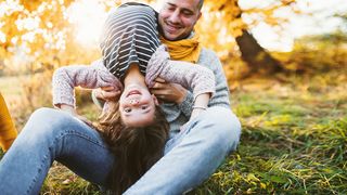 Vater und Tochter toben auf einer Wiese in der Herbstsonne