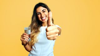 Junge Frau mit Wasserglas zeigt einen Daumen hoch