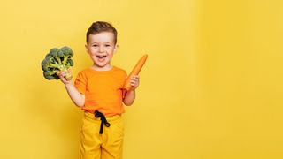 Nutri-Factory Lachender kleiner Junge hält Brokkoli und eine Möhre