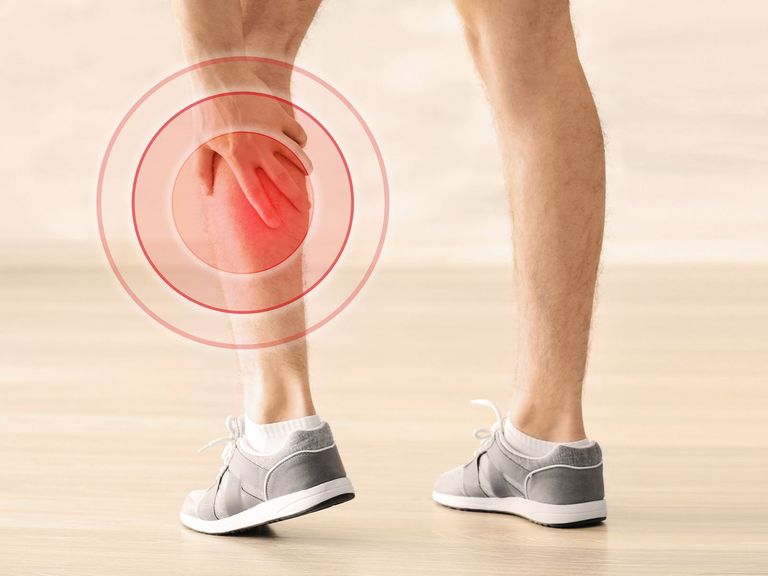 Ein Mann in Turnschuhen fasst sich mit der Hand an die schmerzende Wade