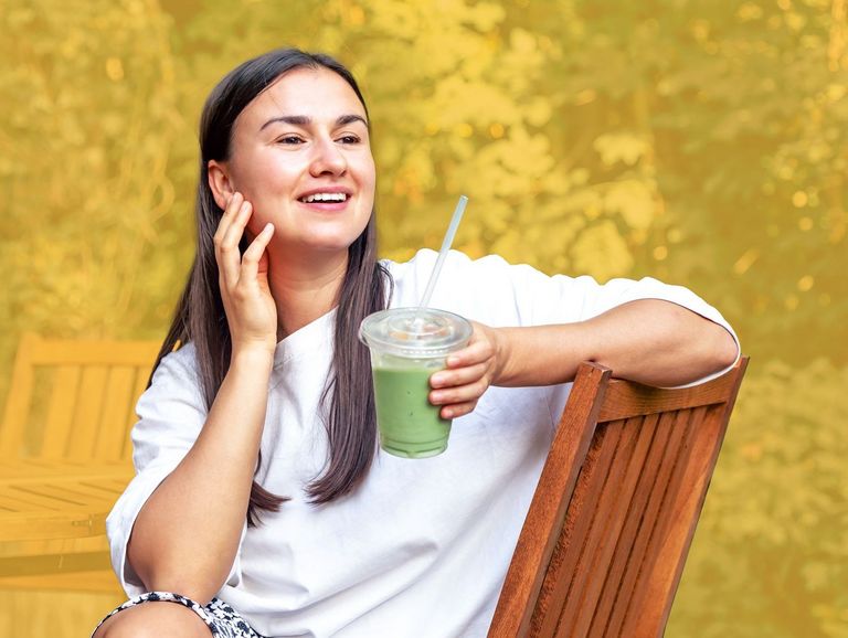 Junge lächelnde Frau hält einen Becher mit Matcha-Tee in der Hand