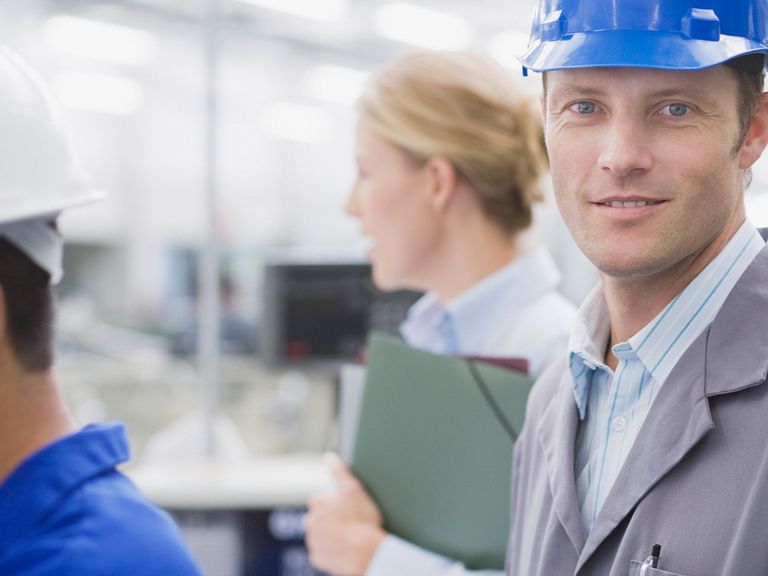 Mitarbeiter in Fertigungshalle schaut in die Kamera