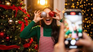 Frau hält sich lachend Weihnachtsbaumkugel vor die Augen