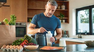 Proteinmaxxing Mann in der Küche bereitet einen Eiweiß-Shake zu
