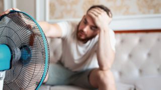 Hitzeerschöpfung Mann im Wohnzimmer vor einem Ventilator sitzend