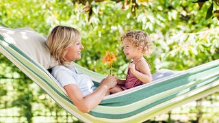 Frau mit einem kleinen Mädchen sitzen in einer Hängematte und freuen sich über eine orangefarbende Blume