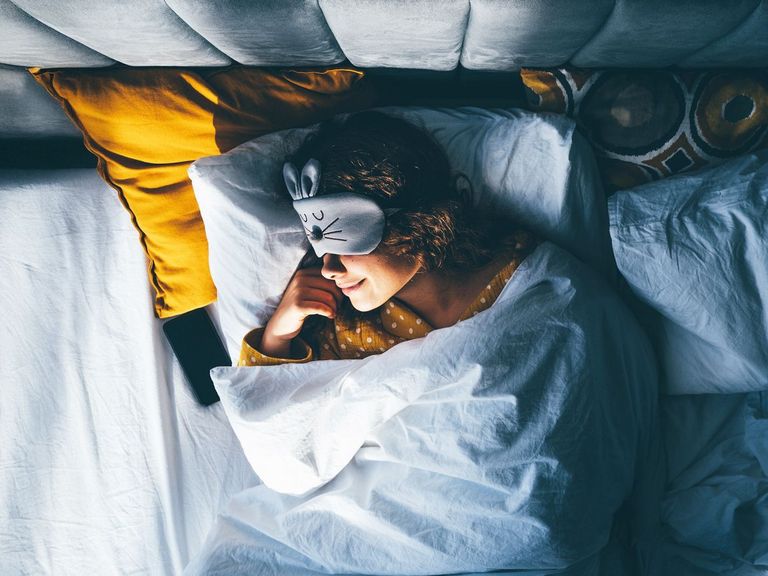 Frau liegt mit einer Augenschlafmaske im Bett und schläft