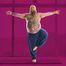 Bärtiger Mann mit Bauch und Tattoos steht auf einem Bein und streckt die Arme seitlich aus