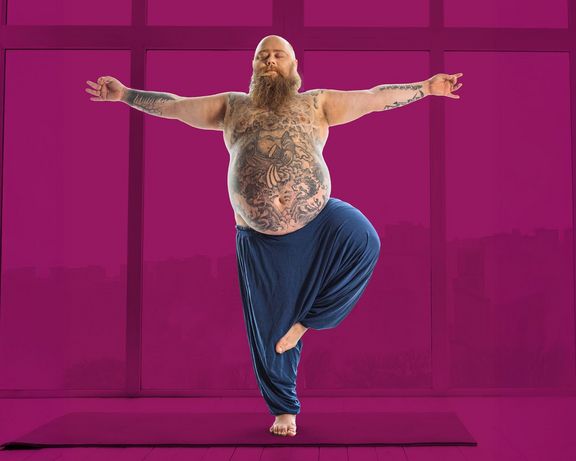 Bärtiger Mann mit Bauch und Tattoos balanciert auf einem Bein, Arme ausgestreckt﻿