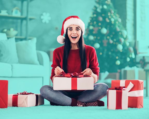 Frau mit Weihnachtsmütze packt mit großen Augen Pakete aus