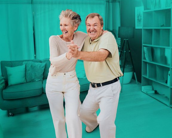 Vorsorgepaket Seniorenpaar tanzt lachend im Wohnzimmer