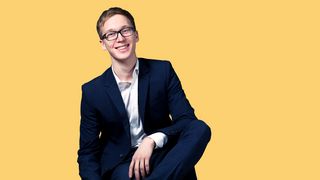 Sitzender Jugendlicher im Anzug mit Brille und gepflegtem Haar