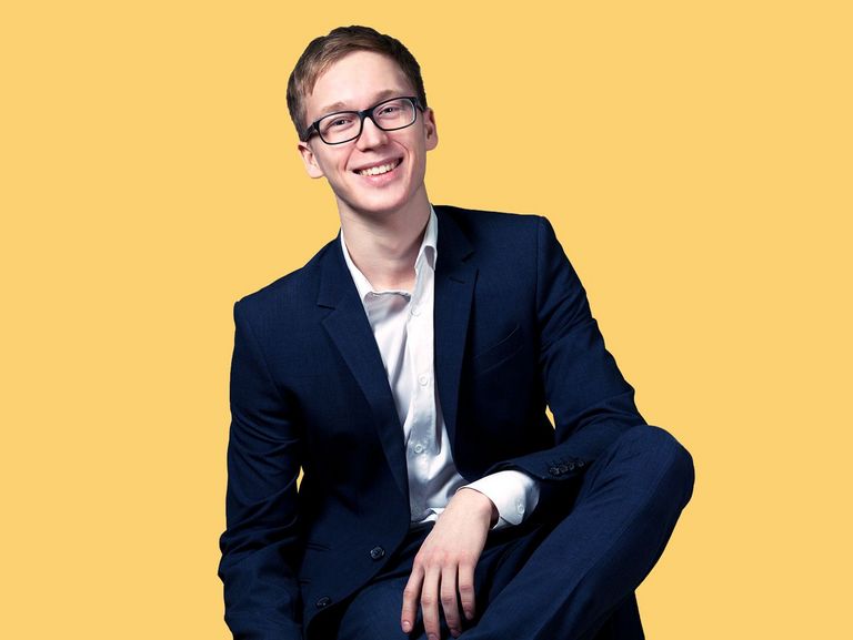 Sitzender Jugendlicher im Anzug mit Brille und gepflegtem Haar