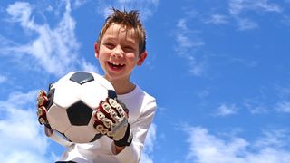Fröhlich lachender Junge mit einem Fußball und Fußballhandschuhen