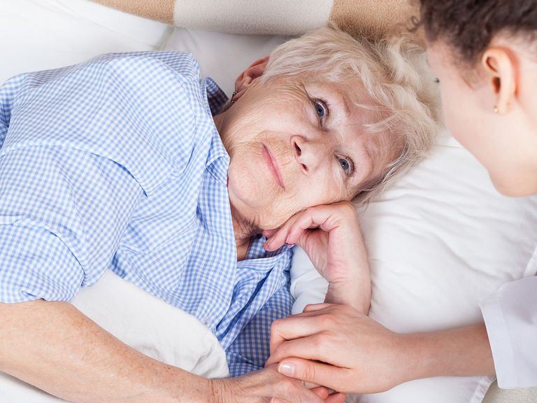 Ältere Frau im Bett wird von junger Pflegerin versorgt