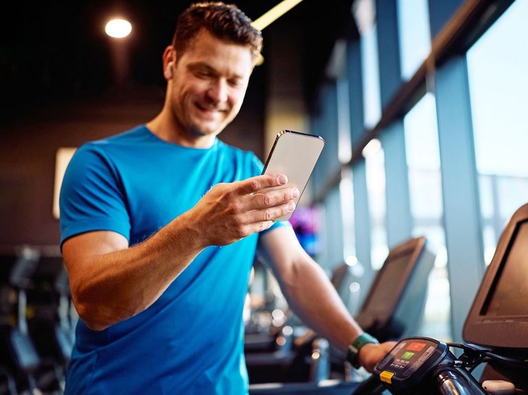 Sportler im Fitnessstudio schaut auf sein Smartphone