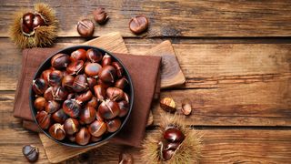 Superfood Esskastanien Holztisch mit einer Pfannen voller Esskastanien