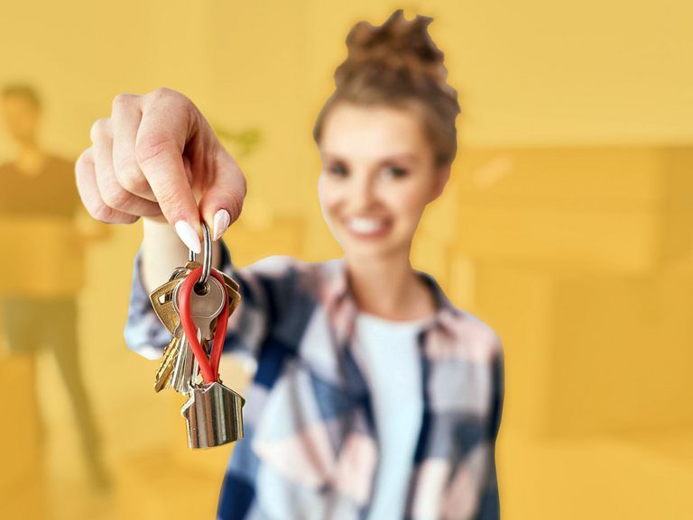 Junge Frau mit Umzugskartons zeigt neuen Schlüssel