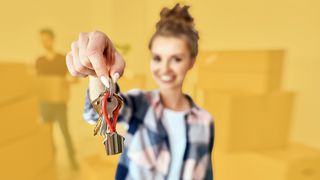 Umzug Junge Frau mit Umzugskartons zeigt neuen Schlüssel