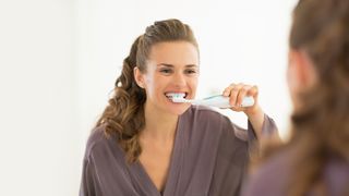 Schwangere Frau putzt vor einem Spiegel die Zähne
