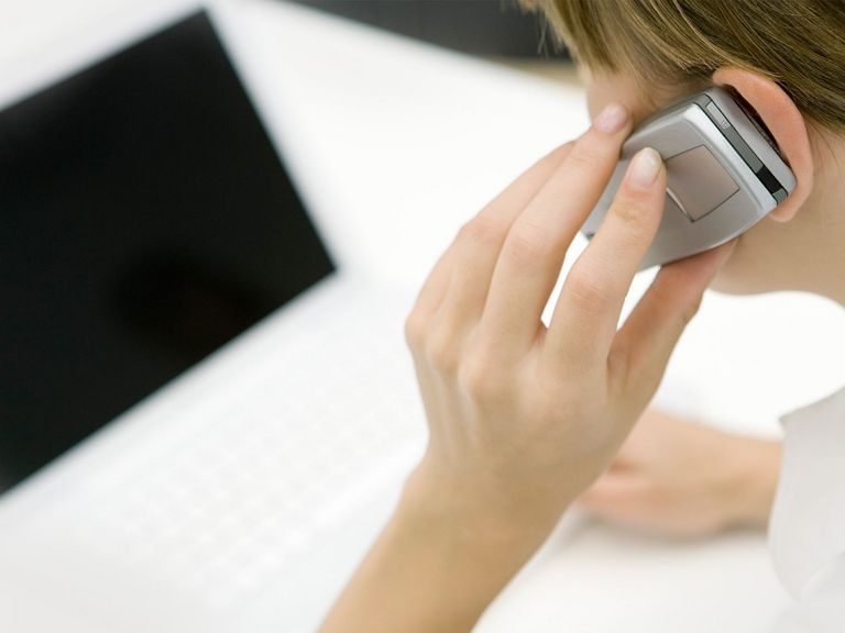 Frau telefoniert am Handy vor Computer