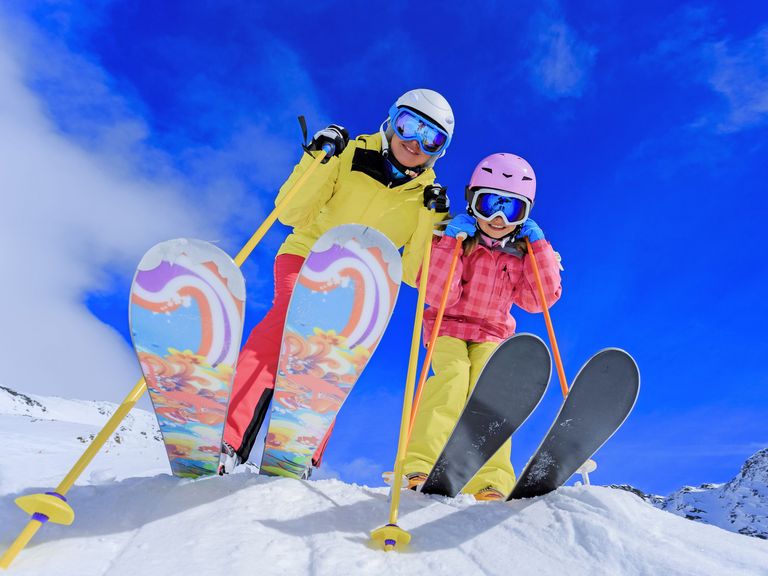Mutter und Tochter in kompletter farbenfroher Skiausrüstung stehen lachend im Schnee
