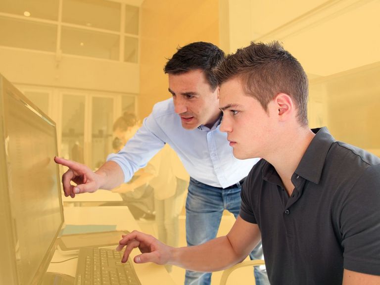 Junger Mann lässt sich am PC-Bildschirm etwas erklären