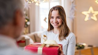 Jugendliche nimmt lächelnd ein weihnachtliches Geschenk von ihrem Vater entgegen