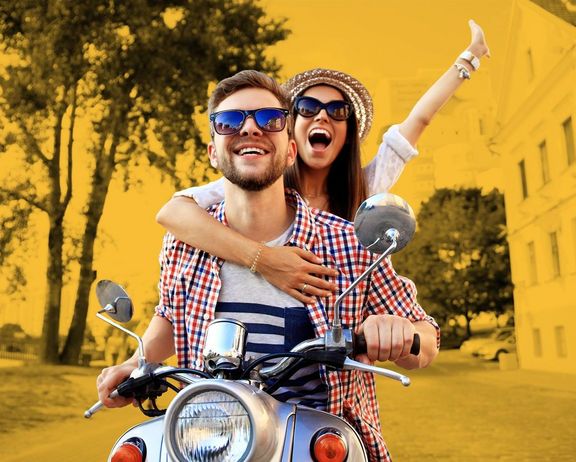 Zwei huttragende und jubelnde Studenten auf einem Roller