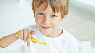 Junge mit einer Zahnbürste in der Hand zeigt in die Kamera