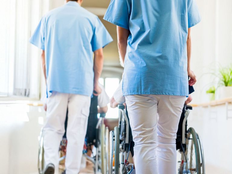 Zwei Stationspfleger schieben Rollstühle mit Pflegebedürftigen