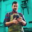 Handwerker in seiner Werkstatt schaut auf sein Smartphone