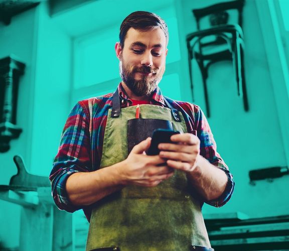 Handwerker in seiner Werkstatt schaut auf sein Smartphone